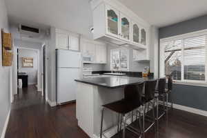 Kitchen with a breakfast bar area, dark hardwood / wood-style floors, kitchen peninsula, white appliances, and white cabinets