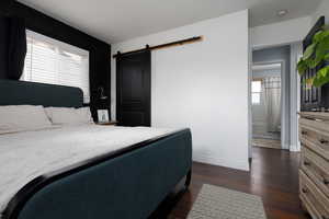 Bedroom with a barn door and dark wood-type flooring