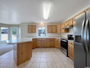 Kitchen featuring appliances with stainless steel finishes, kitchen peninsula, light tile patterned floors, and light brown cabinets