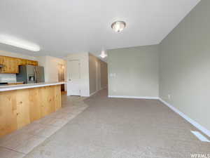 Kitchen featuring stainless steel refrigerator with ice dispenser, light colored carpet, light brown cabinetry, and a breakfast bar