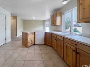 Kitchen with light tile patterned flooring, sink, white dishwasher, and kitchen peninsula