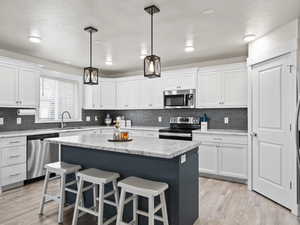 Kitchen with sink, white cabinetry, hanging light fixtures, appliances with stainless steel finishes, and a kitchen island