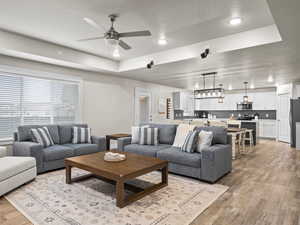 Living room with ceiling fan, a raised ceiling, sink, and light hardwood / wood-style flooring