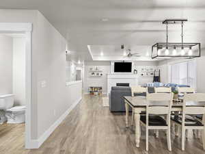 Dining area with rail lighting, ceiling fan, wood-type flooring, a fireplace, and a raised ceiling