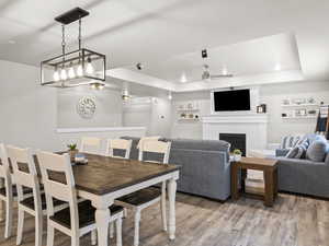 Dining room featuring hardwood / wood-style flooring, a fireplace, a raised ceiling, and ceiling fan