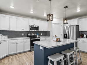 Kitchen featuring light stone countertops, appliances with stainless steel finishes, pendant lighting, and white cabinets