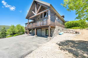 View of front of property with stone siding, asphalt driveway, a garage, and a deck