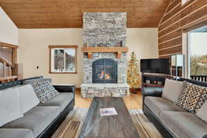 Living room featuring vaulted ceiling, a stone fireplace, a wealth of natural light, and wooden ceiling