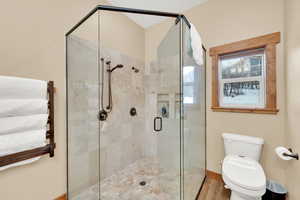 Bathroom featuring wood-type flooring, toilet, and a shower with shower door