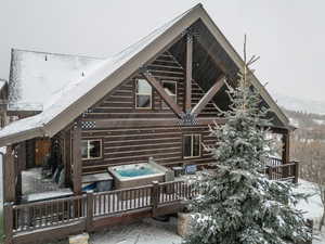 View of snow covered exterior featuring a hot tub and a deck with mountain view