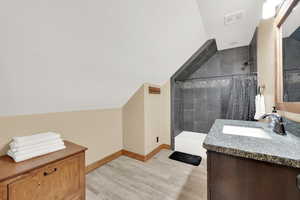 Bathroom with vaulted ceiling, vanity, wood-type flooring, and tiled shower