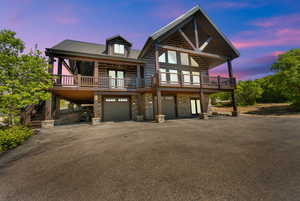 View of front of property featuring stone siding, driveway, an attached garage, a wooden deck, and stairs