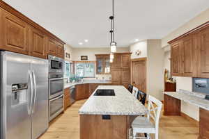 Kitchen with a kitchen bar, light stone counters, decorative light fixtures, a center island, and stainless steel appliances