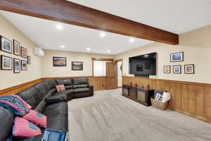 Carpeted living room with beam ceiling, a wall mounted AC, and wood walls