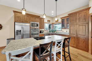 Kitchen with a breakfast bar area, decorative light fixtures, a kitchen island, stainless steel appliances, and light stone countertops