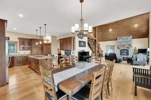 Dining area featuring an inviting chandelier, a stone fireplace, vaulted ceiling, and light hardwood / wood-style flooring