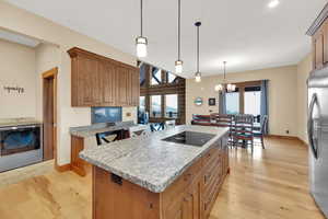 Kitchen with stainless steel refrigerator, hanging light fixtures, a center island, light hardwood / wood-style floors, and washer / dryer