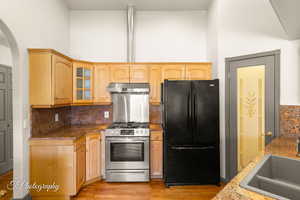 Kitchen featuring black refrigerator, tasteful backsplash, sink, light stone countertops, and stainless steel range with gas stovetop