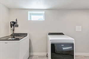 Laundry room with washing machine and clothes dryer, a textured ceiling, and light hardwood / wood-style flooring