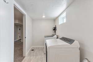 Laundry area featuring separate washer and dryer, a textured ceiling, and light hardwood / wood-style flooring