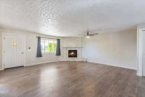 Unfurnished living room with ceiling fan, a textured ceiling, a fireplace, and wood-type flooring