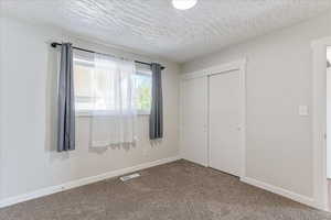 Unfurnished bedroom featuring a closet, a textured ceiling, and carpet flooring