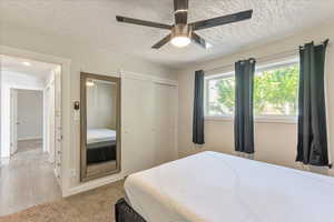 Bedroom with light carpet, ceiling fan, a closet, and a textured ceiling