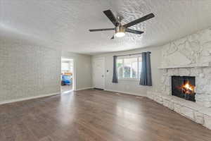 Unfurnished living room featuring a stone fireplace, wood-type flooring, a textured ceiling, and ceiling fan