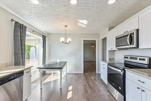 Kitchen featuring pendant lighting, white cabinetry, stainless steel appliances, light stone countertops, and light wood-type flooring