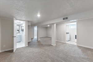 Basement with light colored carpet, washer / clothes dryer, and a textured ceiling