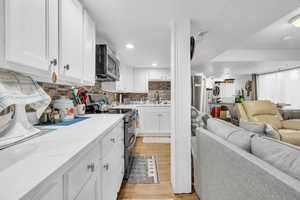 Kitchen featuring light wood finished floors, stainless steel appliances, open floor plan, white cabinetry, and light stone countertops