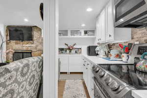 Kitchen featuring glass insert cabinets, appliances with stainless steel finishes, light countertops, light wood-type flooring, and white cabinetry