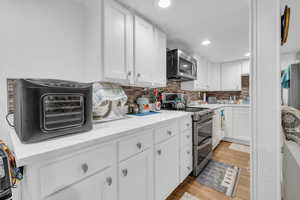 Kitchen featuring light stone counters, stainless steel appliances, white cabinets, light wood-type flooring, and backsplash