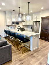Kitchen featuring a breakfast bar area, premium appliances, pendant lighting, light hardwood / wood-style floors, and light great cabinets