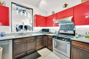 Kitchen featuring sink, light tile patterned floors, appliances with stainless steel finishes, range hood, and decorative light fixtures