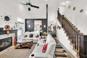 Living room featuring a tiled fireplace, a towering ceiling, track lighting, and ceiling fan