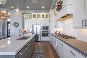 Kitchen with white cabinetry, stainless steel appliances, decorative light fixtures, and sink