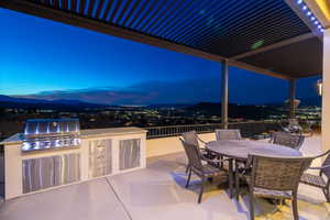 Patio terrace at dusk with an outdoor kitchen, grilling area, and a mountain view