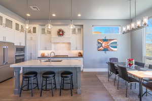 Kitchen featuring sink, appliances with stainless steel finishes, backsplash, white cabinets, and a center island with sink