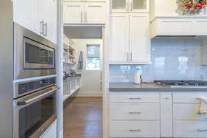 Kitchen with white cabinetry, backsplash, stainless steel appliances, and dark hardwood / wood-style floors