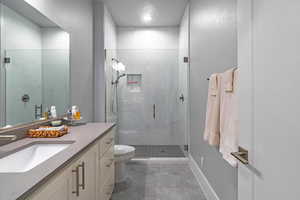 Bathroom featuring a shower with door, vanity, tile patterned flooring, and toilet