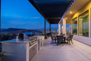 Patio terrace at dusk with a mountain view, grilling area, and exterior kitchen