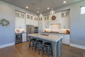 Kitchen featuring an island with sink, sink, white cabinets, wine cooler, and stainless steel appliances