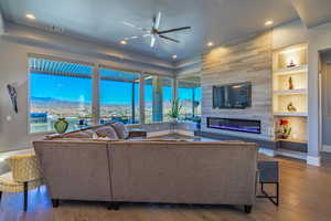 Living room featuring hardwood / wood-style floors, built in features, a fireplace, ceiling fan, and a mountain view