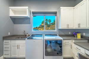 Clothes washing area with cabinets, washer and dryer, and sink