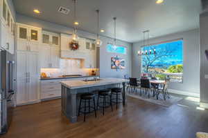 Kitchen with sink, a center island with sink, white cabinets, and decorative light fixtures