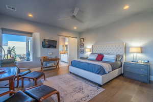 Bedroom with ensuite bathroom, a barn door, ceiling fan, and light wood-type flooring