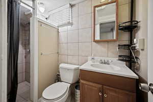 Bathroom with tile walls, vanity, curtained shower, and toilet