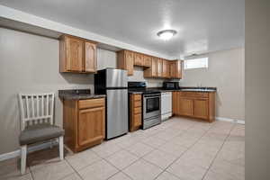 Kitchen with sink, light tile patterned flooring, a textured ceiling, and appliances with stainless steel finishes