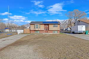 Raised ranch featuring a mountain view, a front lawn, and solar panels